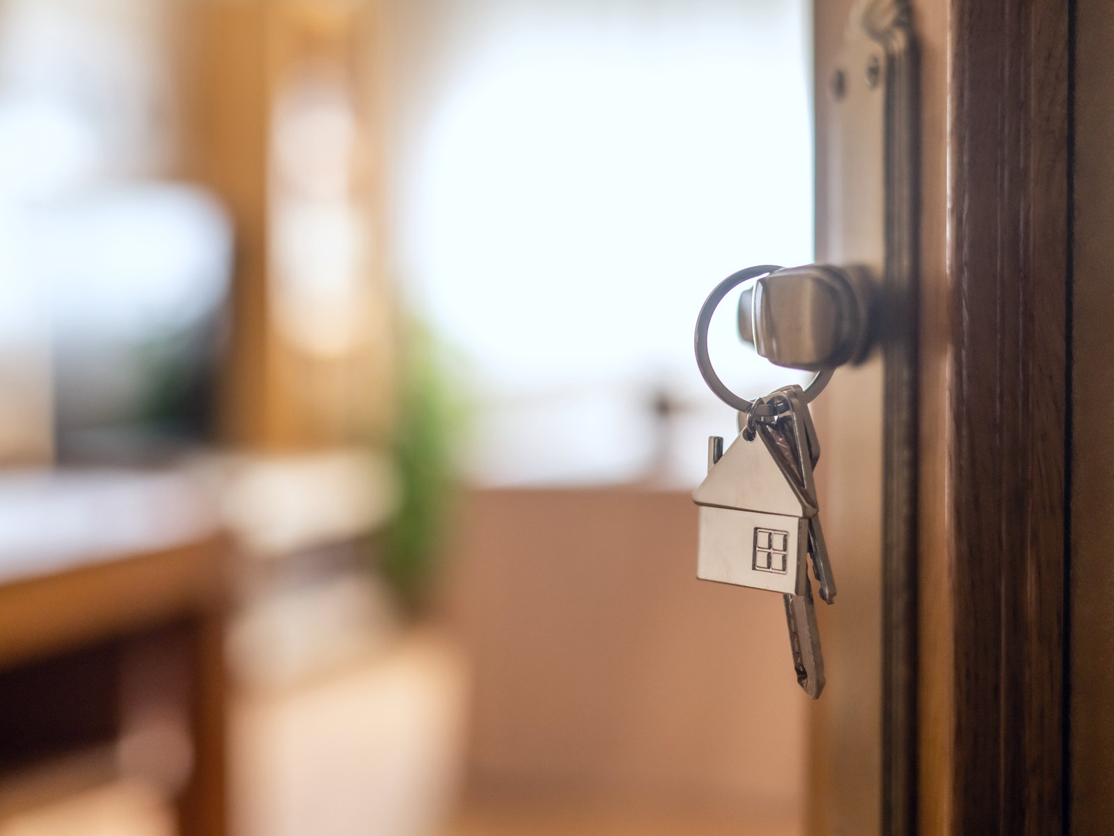 House keys on a wooden keyring hanging from a door lock, a warm room beyond