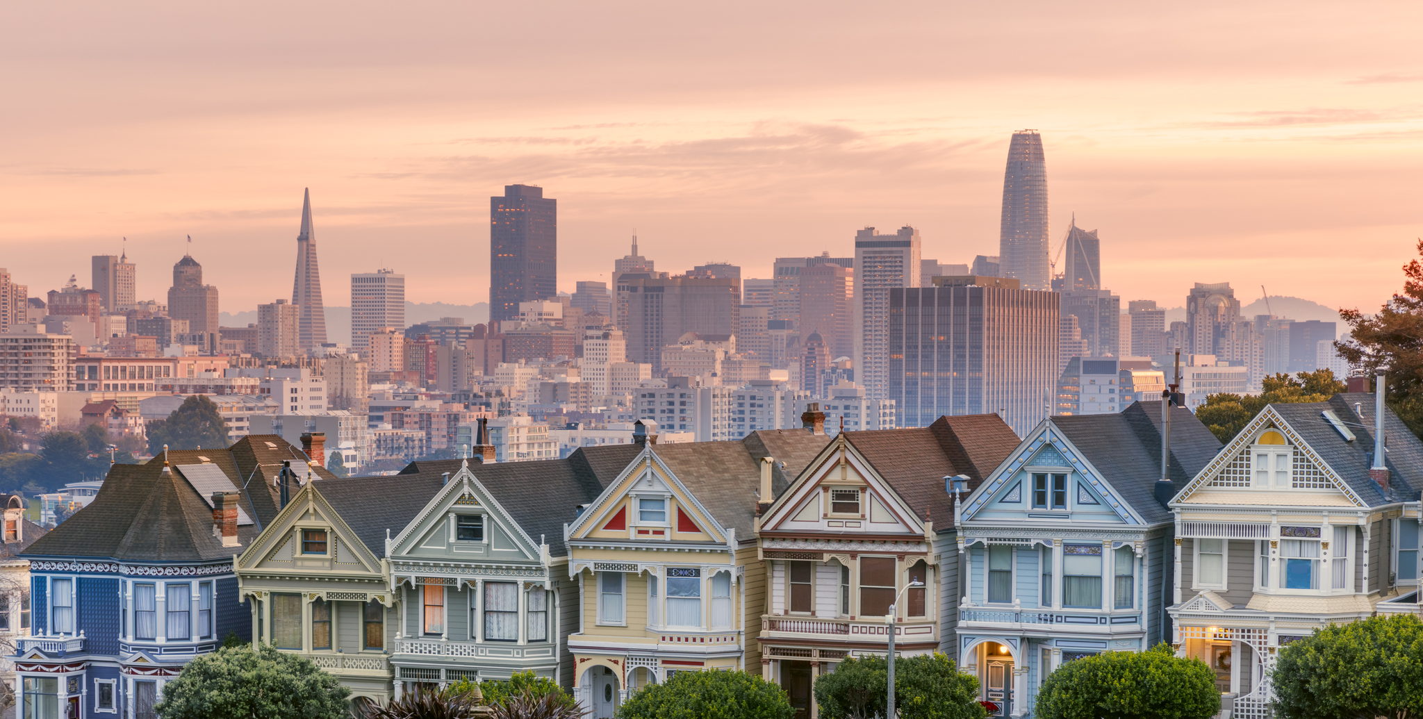 Victorian row houses in San Francisco at sunrise, city skyline behind